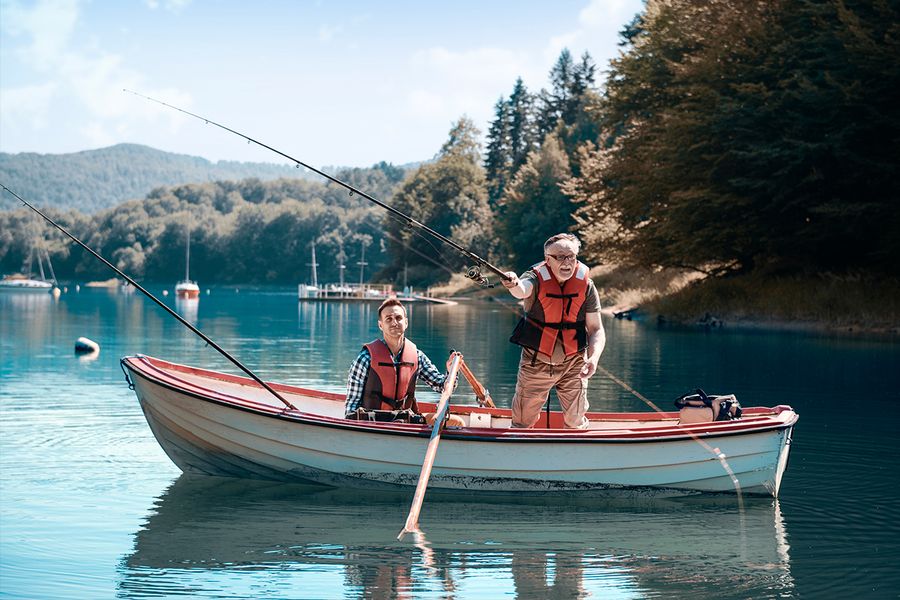 A photo of an older man and his son fishing in a boat on a lake.