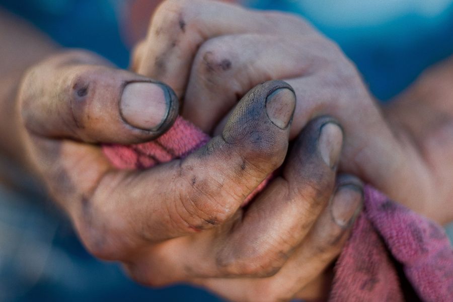 A close-up photo of a pair of man’s hands, covered in soil, holding a cloth.